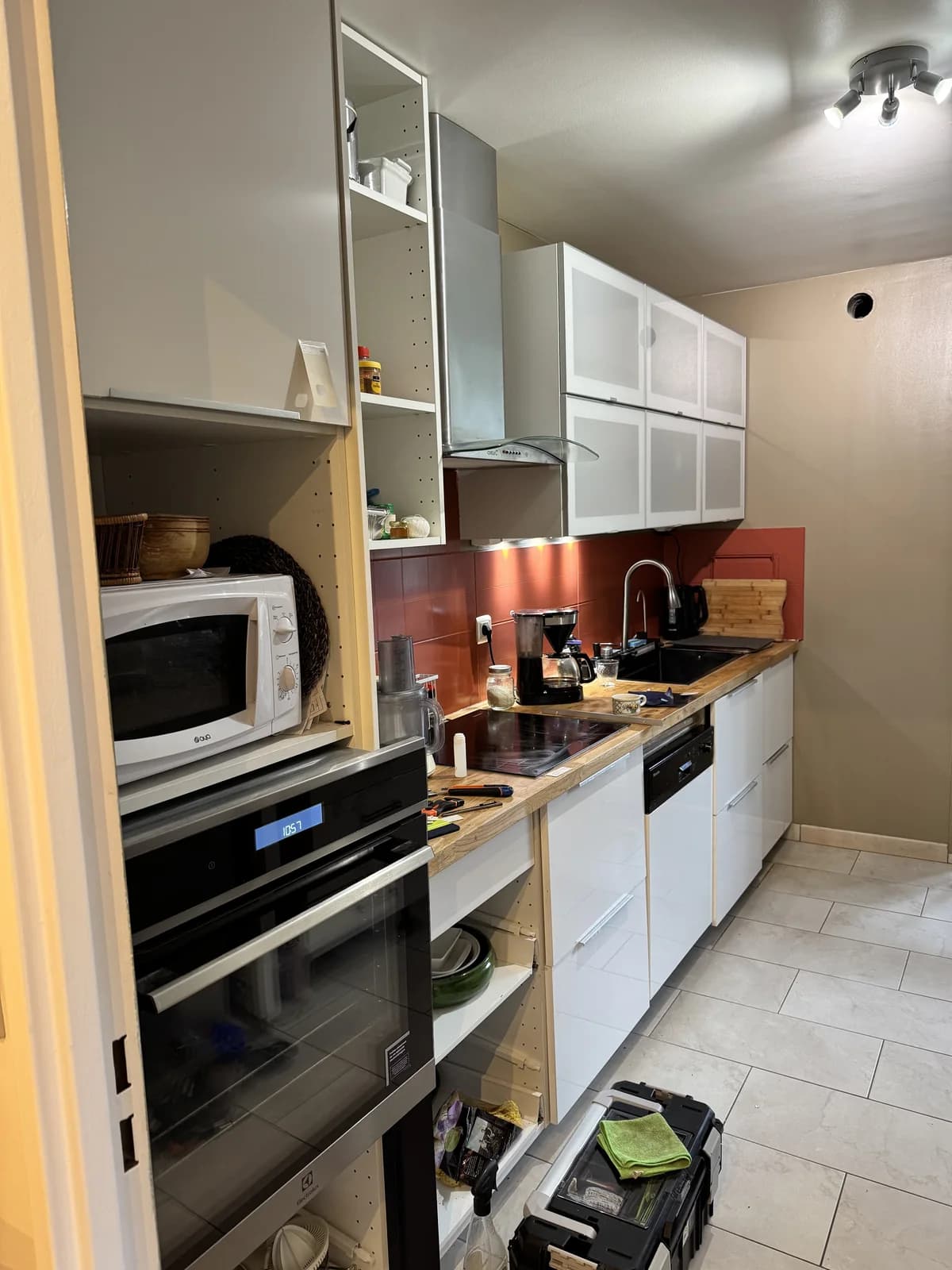 Avant : Cuisine avant rénovation, avec façades claires et vitrées, plan de travail bois et crédence rouge.